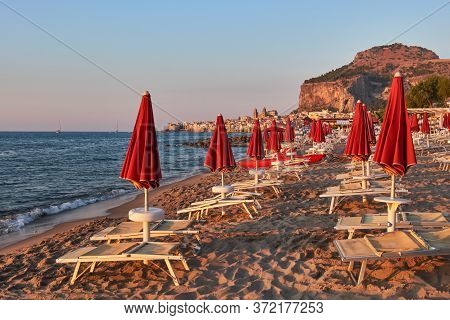 Empty Beach Cefal, In Dusk Atmosphere Closed Parasols In Front Of The Skyline Of Cefal With Its Famo
