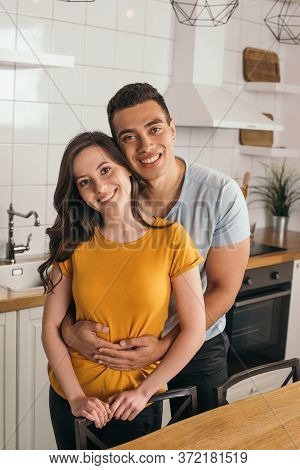 Mixed Race Man Embracing Smiling Girlfriend In Kitchen