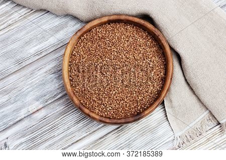 Raw Roasted Buckwheats In Round Wooden Bowl On Light Wood And Coarse Cloth. Russian Grechka. Organic