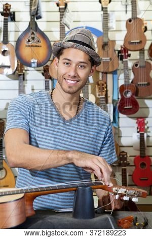 Portrait of happy man restringing guitar in music store