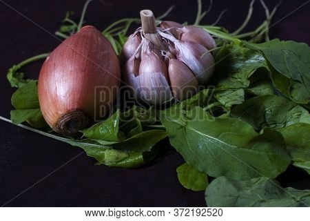 An Onion A Garlic And Arugula On A Dark Table