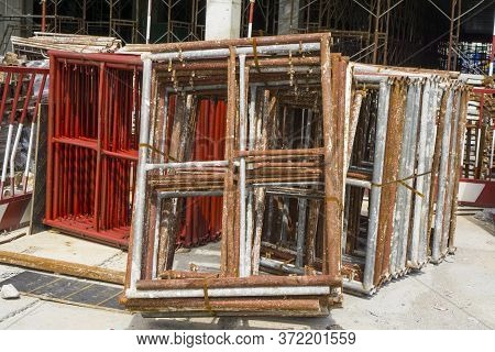 A Pile Of Steel Scaffolding With Brown Rust On The Cocrete Floor In Front The Building