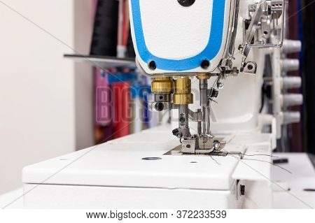 A Professional Sewing Machine Is In The Workshop. Against The Background Of Various Devices And What