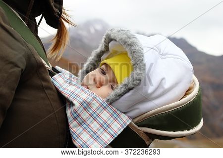 Portrait Of Little Girl In Ergo Carrier With Her Mother On A Background Of Autumn Mountains.