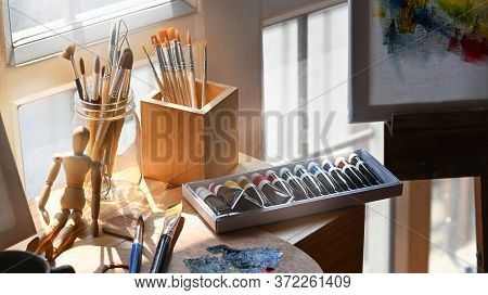 Photo Of Artist Equipment Putting On Wooden Working Table. Paint Brush, Oil Color, Palette, Puppet, 