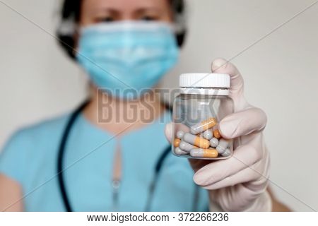 Doctor With Pills, Woman In Medical Mask And Latex Gloves Giving Transparent Bottle Of Capsules. Con