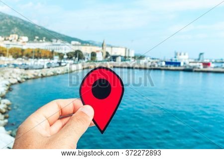 the hand of a young caucasian man with a red marker pointing the port of Bastia, in Corsica, France, with the commercial port on the right and the Notre-Dame de Lourdes church in the background