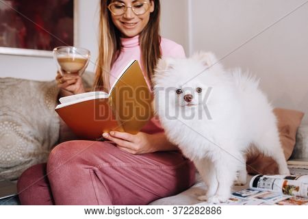 A Girl In Pajamas At Home Reads A Book With Her Dog Spitzer, The Dog And Its Owner Are Resting On Th