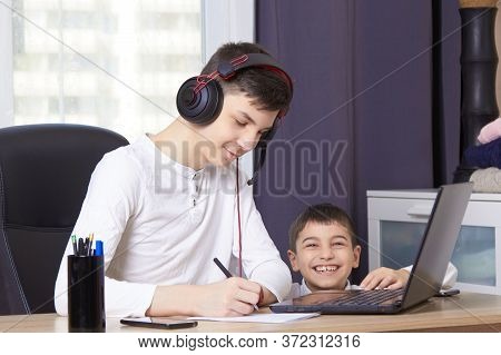 Teenager Looks At A Laptop And Writes Down A Task And Children Interfere With Learning