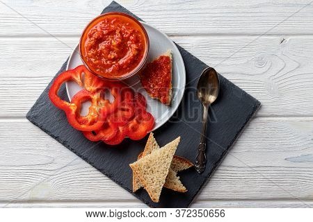 Ajvar Or Pindjur Red Vegetable Sauce, Paprika Pepper On A Black Board And Wooden Table. Serbian Trad