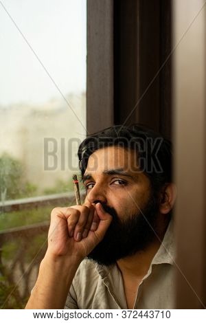 A Bearded Jobless Indian Man Wearing Kurta Pyjama Smoking Weed Rolled In A Paper. He Is Staring At C