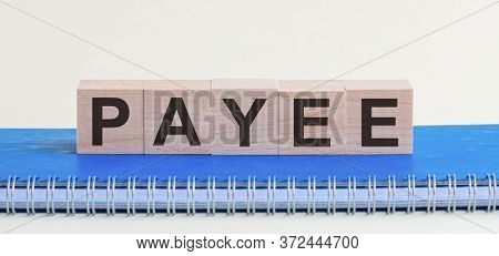 Payee - A Word Made Of Wooden Blocks With Black Letters, A Row Of Blocks Is Located On A Blue Notepa