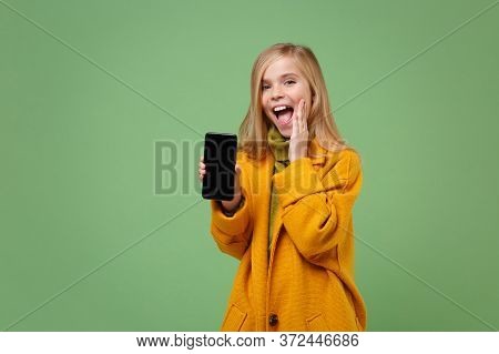 Excited Little Kid Girl 12-13 Years Old In Yellow Coat Isolated On Green Wall Background. Childhood 