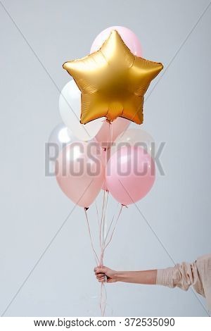 Composition Of White, Pink, Transparent Helium Balloons And Gold Star In The Hand Of A Woman On A Wh