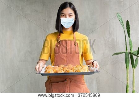 Woman In Medical Mask Holding Baking Tray With Choux Cream Sme Concept.