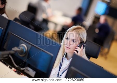 Female security guard operator talking on the phone while working at workstation with multiple displays Security guards working on multiple monitors