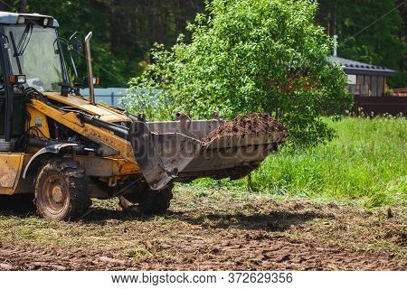 Clearing And Leveling A Private Land Plot. Yellow Excavator Driven Earth In A Wide Bucket