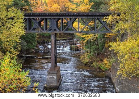Autumn Background. Railroad Bridge Over A River With A Waterfall In The Background Surrounded By Vib