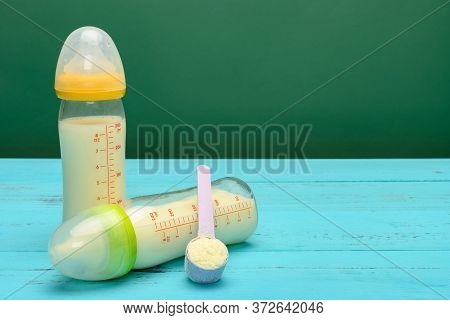 Two Glass Baby Bottles With Powdered Milk And A Scoop Nearby