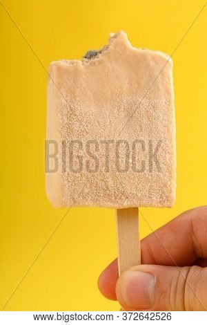Hand Holding A Milk Tea Flavor Popsicle With Couple Of Bites On Yellow Background
