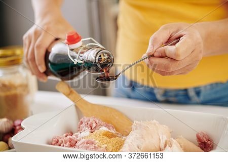 Hands Of Person Adding Spoon Of Soy Sauce Into Bowl With Ground Meat