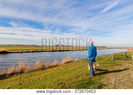 Landscape river the Eem in the Netherlands with senior man and dog
