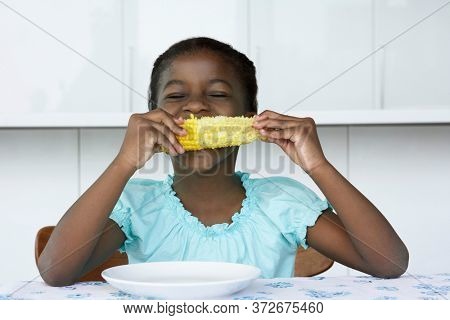 Girl (5-6) sitting at table eating corn cobb