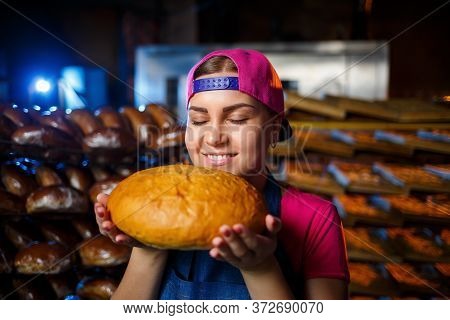 The Stage Of Baking In A Bakery. Portrait Of A Baker Girl With Bread In Her Hands Against The Backgr