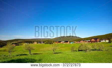 Small Village Of Mountain Huts In A Green Colorful Hilly Landscape With Snezka Mountain In The Backg