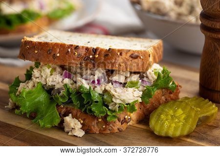 Tuna Fish Salad And Lettuce Sandwich On Multiseed Bread With Sliced Pickles On A Wooden Cutting Boar