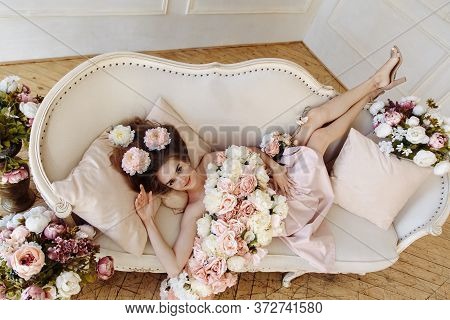 The Beautiful Girl Is On The Sofa With Flowers. The Amazing Girl With Flowers In View From Above. Th
