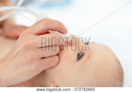 Closeup Mother Hand With Aspirator Medical Tool Cleaning Runny Nose Of Cute Infant Newborn Baby Boy 