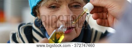 Close-up Of Unhealthy Grandma Holding Cup With Medication. Hand Of Male Person Adding Cannabinoid Oi