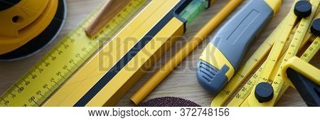Close-up Of Level Ruler Pencil And Box Cutter On Wooden Table. Yellow Sander For Renovation Works. R