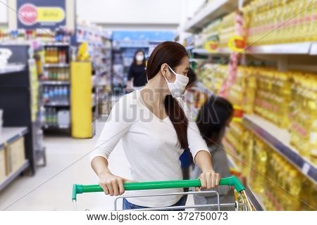 Asian Woman Wear Face Mask Push Shopping Cart In Suppermarket Departmentstore. Girl Choosing, Lookin