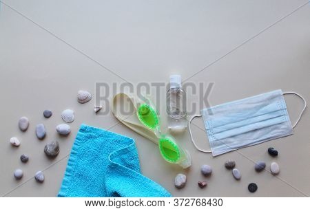 Swimming Glasses, Towel, Pebbles, Medical Mask And Antiseptic On A Light Background. The Tourist Cri