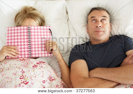 Ennuyé de recherche Senior homme couché dans son lit à côté du livre de lecture Senior femme