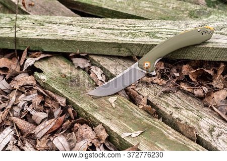 Knife With A Green Handle On Green Wooden Boards. Photo Of A Knife In The Forest.