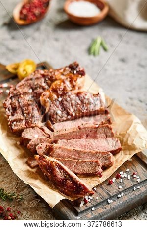 Classic ribeye steak served in waxed paper on wooden cutting board. Cut against grain beef steak. Roasted beef steak with yellow chilli pepper slices and salt crumbs. Rustic spoon and spice bowl