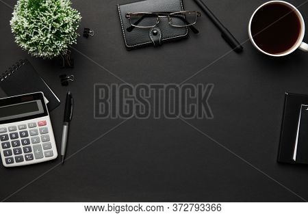 Top view of modern black office desk with calc, notebook, pen and a lot of things. Flat lay table layout. Copy space for text.