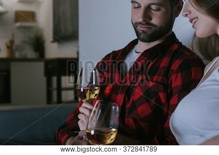 View Of Smiling Girl And Handsome Boyfriend Sitting On Sofa With Glasses Of White Wine