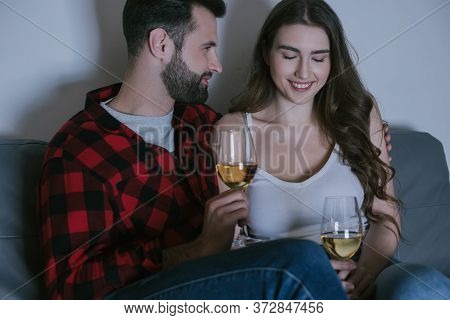 Man And Smiling Girlfriend Sitting On Sofa With Glasses Of White Wine