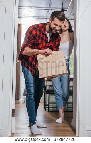 Man Looking In Paper Bag With Delivered Food Near Attractive Girlfriend