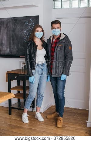 Young Couple In Protective Masks And Latex Gloves Looking At Camera While Standing Near