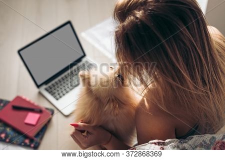Beautiful Woman Works From Home With Dokuments And Laptop. The Dog Helps Her. Girl Kisses Her Pomera