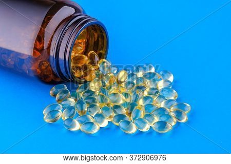 Brown Glass Bottle With Yellow Capsules Vitamin D3 On Blue Background.