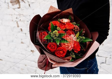 Bouquet Of Flowers In Burgundy Package In The Hands Of A Woman Florist On Background A White Brick W