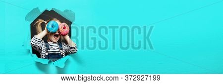 Happy cute boy is having fun played with donuts on black background wall. Bright photo of a boy. Colored donuts