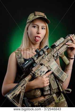 A Sexy Girl In Military Airsoft Overalls Poses With A Gun In Her Hands On A Dark Background
