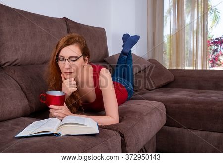 Woman Sitting Comfortably At Her Living Room On A Couch And Reading A Book